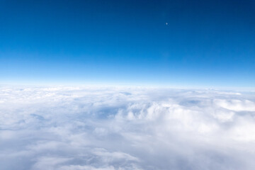 Fototapeta na wymiar View from airplane window of white, fluffy clouds below and deep indigo sky overhead