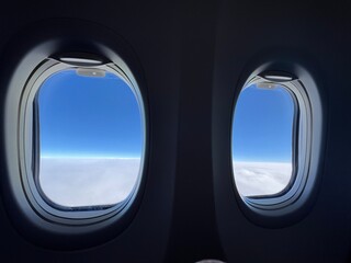 Looking through silhouetted airplane windows at white, fluffy clouds below and deep indigo sky overhead