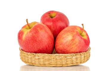 Three juicy red apples on a straw tray, close-up, isolated on a white background.
