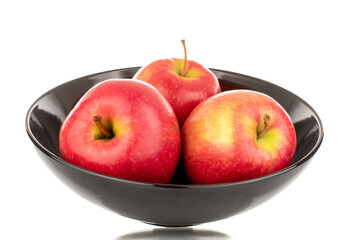 Three juicy red apples in a black ceramic plate, close-up, isolated on a white background.