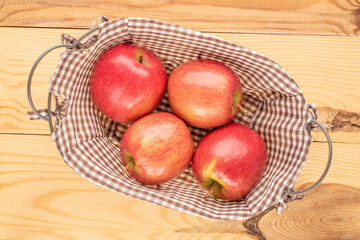 Four juicy red apples in a basket on a wooden table, close-up, top view.