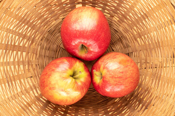 Three juicy red apples in a straw bowl, close-up, top view.