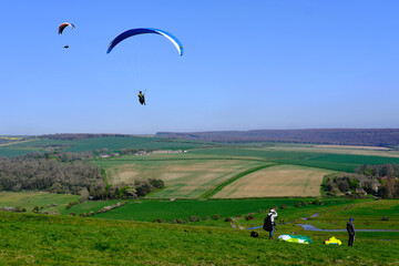Eastbourne, UK. 16 April 2022. Paragliding concept, group of paragliders flying in countryside against clear blue sky. Low angle view.