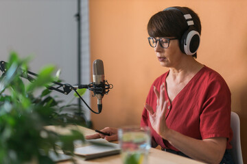 Mature woman making podcast recording for her online show. Attractive business woman using...