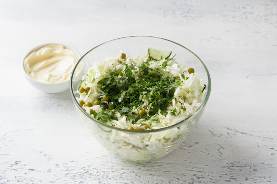 Glass bowl of cabbage salad with cucumbers, green peas, chopped herbs and mayonnaise dressing. Cooking delicious homemade salad. Step-by-step instruction. Step 3
