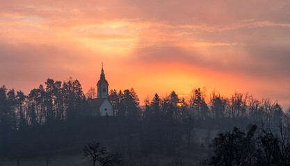 Fototapeta na wymiar Vivid sunrise over the church on a misty morning on Bled