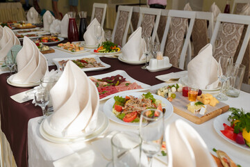 Festive table with appetizers. Salads, cheese and meat plates with vegetables and greenery. Empty glasses, plates, chairs for guests