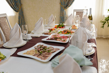 Festive table with appetizers. Salads, cheese and meat plates with vegetables and greenery. Empty glasses, plates, chairs for guests