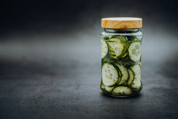 Green cucumber cucumber salad in a screw-top glass jar with a wooden lid with a dark background