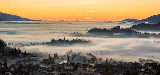 Church and villages hiding in the early morning fog. A misty sunrise in the countryside.