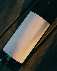 closeup of blank white label mockup on  wine black bottle on wooden background in the rays of the...