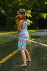 Naklejka premium Happy six year old girl playing with a water sprinkler in the summer sunlit park