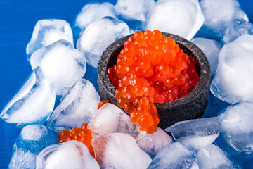 Red salmon caviar in a black cup with ice cubes with a blurred background. Close-up