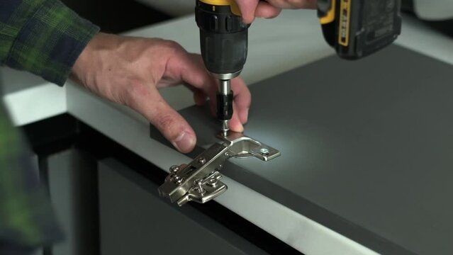 Furniture maker uses a screwdriver to attach hinge to a door of a cabinet. New furniture assembling