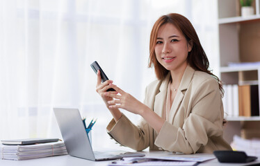 Asian Businesswoman uses a mobile phone and works on laptop computer in the modern home office.