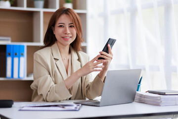 Asian Businesswoman uses a mobile phone and works on laptop computer in the modern home office.