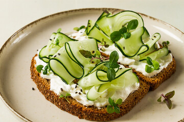 Breakfast, cereal bread sandwiches, cream cheese, sliced cucumber, with micro greenery on a light table, close-up, top view, selective focus, no people,