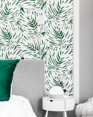 A bedroom detail shot with a green and white wallpaper, a white nightstand, and a light mounted on the wall.