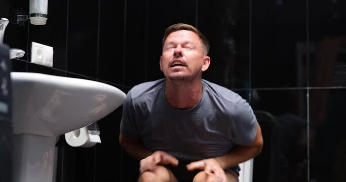 Emotional man sits in toilet and screams in pain and smiles with relief and joy