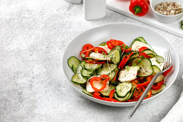 Mix organic salad with sliced cucumbers, feta cheese, sweet peppers in a white plate. Fresh green snack. Keto diet. Vegetarian food.