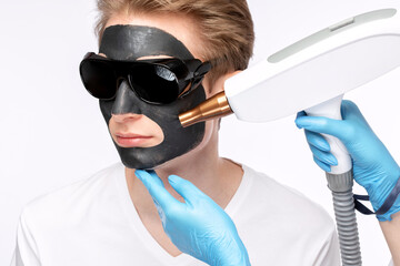 Beautician doing carbon peeling procedure to handsome guy in beauty salon. Hardware male cosmetology.