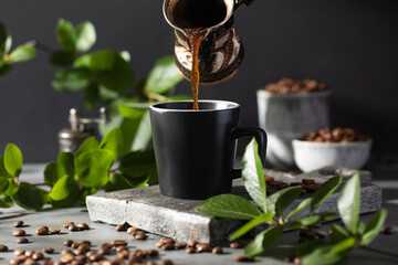 Coffee is poured into a black mug from a metal cup on a dark background.