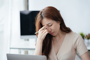 Young business woman stressed and headaches while working on laptop in office space.