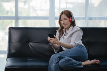 Obraz premium Happy woman is listening music via headset and smartphone at home or office space.