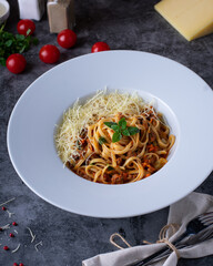 Italian Pasta Bolognese on a white plate with ingredients on a dark background. restaurant menu