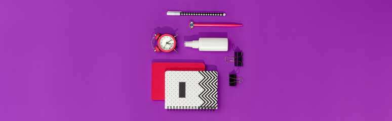Notepads, pens and alarm clock on purple modern table