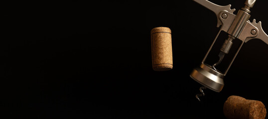 Metal corkscrew and wine corks close-up on the black backdrop.