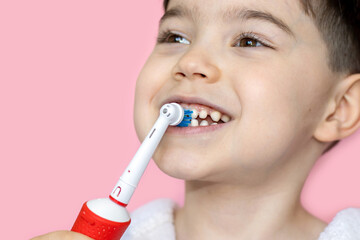 cute little boy using electric toothbrush for daily teeth cleaning.pink background,close up,wide...