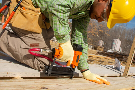 bricklayer on top of a roof nailing a piece of wood with a nail machine - PHOTO SESSION: WORK IN CONSTRUCTION