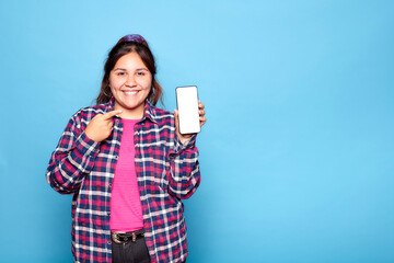 Young curvy latina woman smiling pointing finger at mobile phone in her hand. Indoor studio shot...