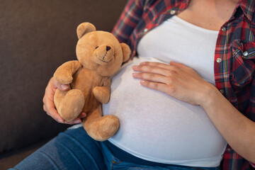 Pregnant woman is lying on bed on her back with a Teddy bear in her hands closeup