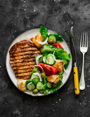 Barbecue pork chop and Italian panzanella salad on a dark background, top view. Mediterranean cuisine concept