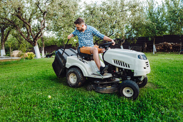 Gardener worker using lawn tractor and cutting grass through garden