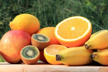 A group of ripe fruits photographed with selective focus. Fruit harvest on nature background. Oranges, kiwi, lemons, apple, bananas, some are cut