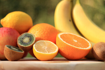 A group of ripe fruits photographed with selective focus. Fruit harvest on nature background. Oranges, kiwi, lemons, apple, bananas, some are cut