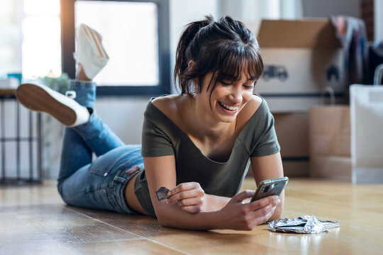 Young beautiful woman with mobile phone while eating a piece of chocolate lying on the floor in her new house.