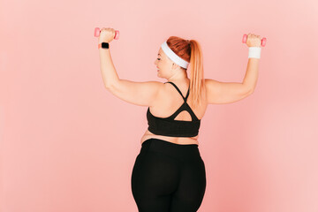 Rear view young woman with plus size body doing exercises with dumbbells