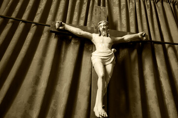 Old wooden crucifix of Jesus Christ isolated on drapery background in medieval church. Sepia...