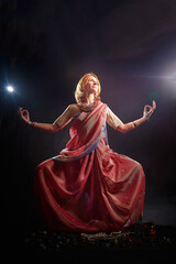 A beautiful adult skinny European blonde woman in a beautiful Indian sari does yoga exercises on a black background in the studio. Sporty romantic girl model posing in a photo shoot