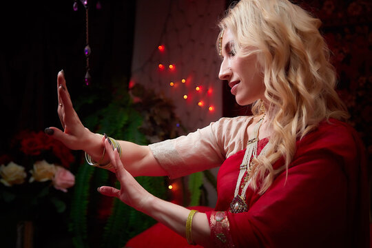 A beautiful European girl looking like an Arab woman in a red room in a harem. Photo shoot of an oriental style odalisque. A model poses in a sari as an indian woman in india