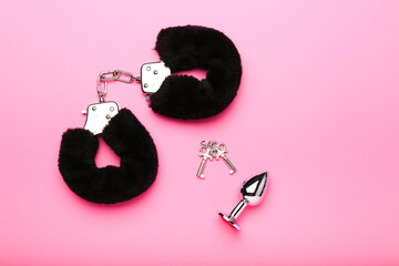 black fluffy handcuffs and sex toy on a pink background - obrazy, fototapety, plakaty