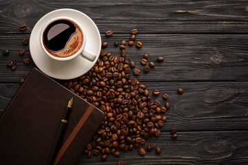 Cup of coffee with coffee grains and notepad on dark boards