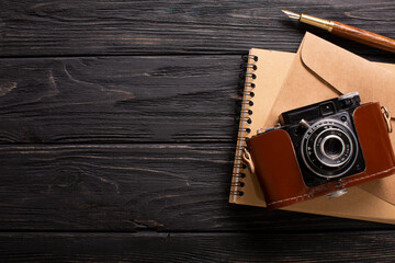 An envelope, a beautiful camera and a notebook with a pen on a black wooden background with a place for an inscription