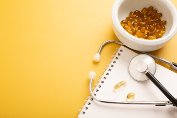 Notepad, vitamins, pills and stethoscope on a yellow background. Place for text
