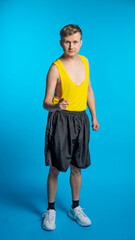 lean sportsman in a yellow t-shirt and black shorts on a blue background. funny sportsman pointing at us