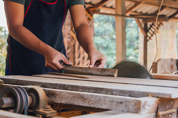 Asian carpenter is using a circular saw to cut wood to construct a storage box on a desk table at his factory. Working as your own boss at home concept